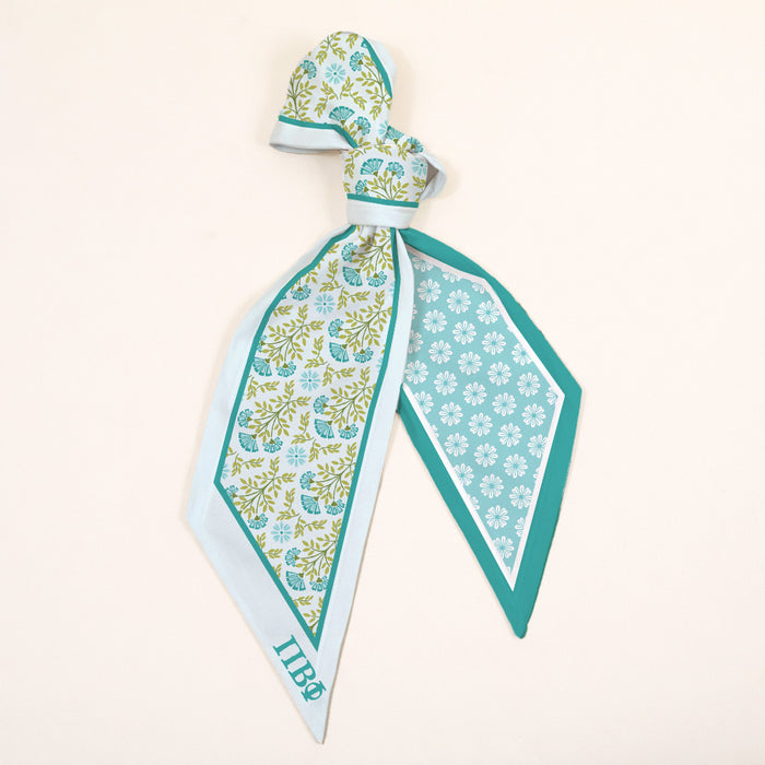 The Darling Effect Pi Beta Phi Twirl & Tie Scarf Accessory features blue and green floral and geometric designs on a light cream background, teal-bordered edges, and IHB initials in one corner for a boutique touch.