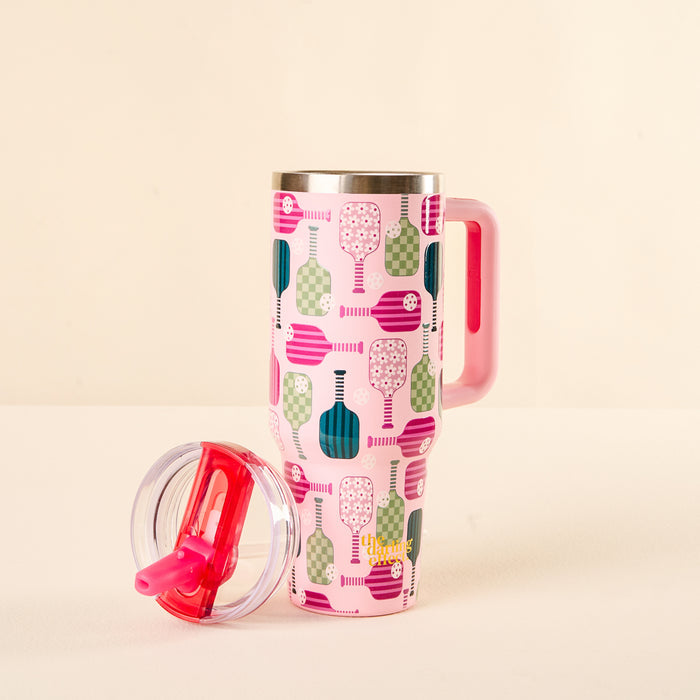 The-darling-effect Pickleball Party 40 oz Lifestyle Flip Straw Tumbler is tall and pink with a handle and colorful pickleball paddle pattern. A clear, leak-resistant lid with a red slider rests in front on a light surface against a beige background.