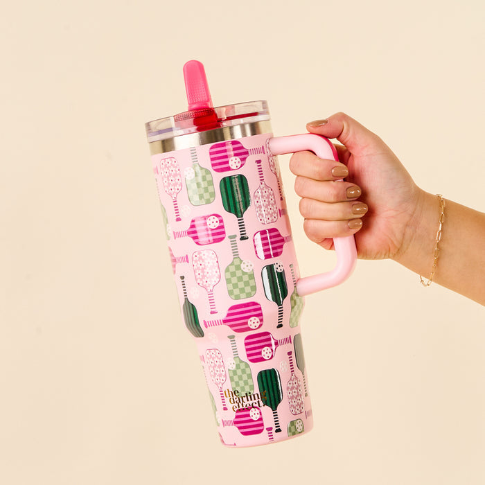 A hand holds the-darling-effect Pickleball Party 40 oz Lifestyle Flip Straw Tumbler, featuring a handle, a leak-resistant red flip straw lid, and a vibrant green and pink pickleball paddle pattern.