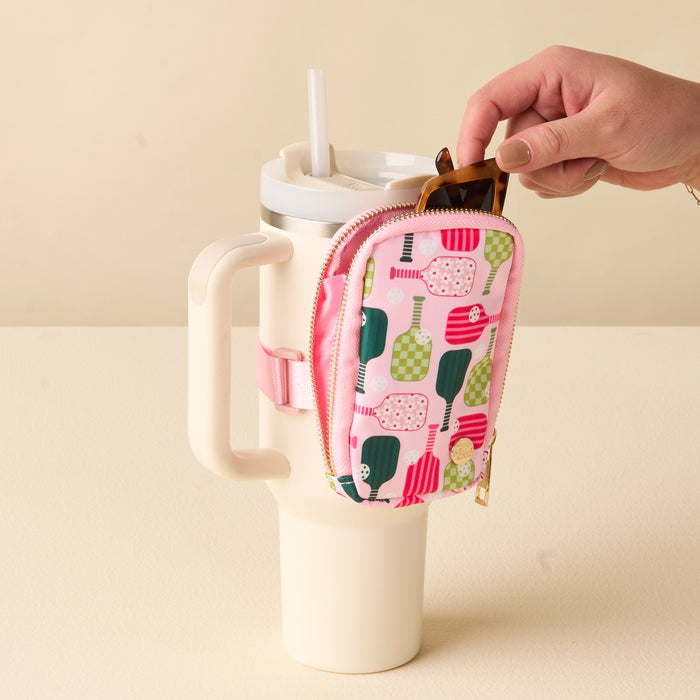 A hand puts sunglasses into the-darling-effect Pickleball Party Tumbler Fanny Pack—a colorful, water-resistant zippered pouch with a paddle pattern—attached to a large white tumbler with a straw.