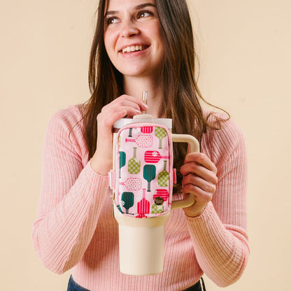 A woman in a pink sweater smiles while holding the-darling-effect's Pickleball Party Tumbler Fanny Pack—a large insulated tumbler with a stylish, water-resistant pink pouch featuring pickleball paddles.