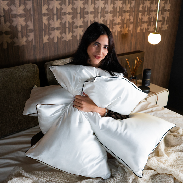 a woman sitting on a bed and holding multiple silkow Pillowcases S22 100% Pure Silk Satin With Narrow Edge