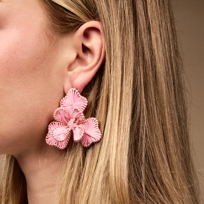 Close-up of a woman's ear wearing The Darling Effect’s Pink Main Character Earrings—large, pink, floral-shaped boho earrings with gold trim. Her blonde hair peeks through; perfect lightweight statement for everyday wear.
