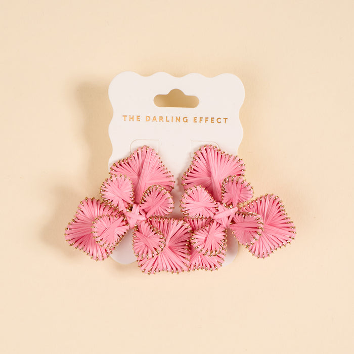The Darling Effect Pink Main Character Earrings—pink, woven floral boho earrings with gold accents, shown on a branded white card against a beige background—make the perfect lightweight accessory for everyday wear.