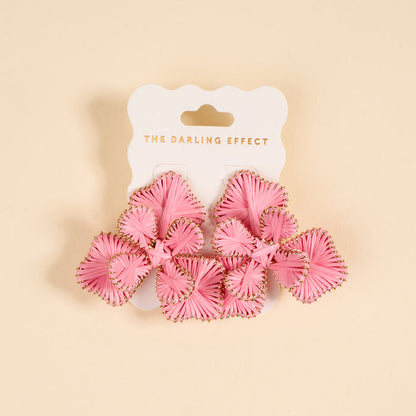The Darling Effect Pink Main Character Earrings—pink, woven floral boho earrings with gold accents, shown on a branded white card against a beige background—make the perfect lightweight accessory for everyday wear.
