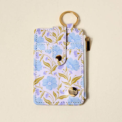 The Darling Effect’s Poppin’ Petals Aqua Keychain Wallet is a pastel slim wallet with gold hardware, blue floral and green leaf print, zipper pocket, snap closure, and a round keyring to use as a keychain wallet.