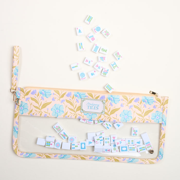 The Darling Effect’s Poppin' Petals Aqua Mahjong Tile Keeper Pouch rests on a cream surface, with Mahjong tiles scattered above and inside its transparent section—ideal for organizing game night essentials.