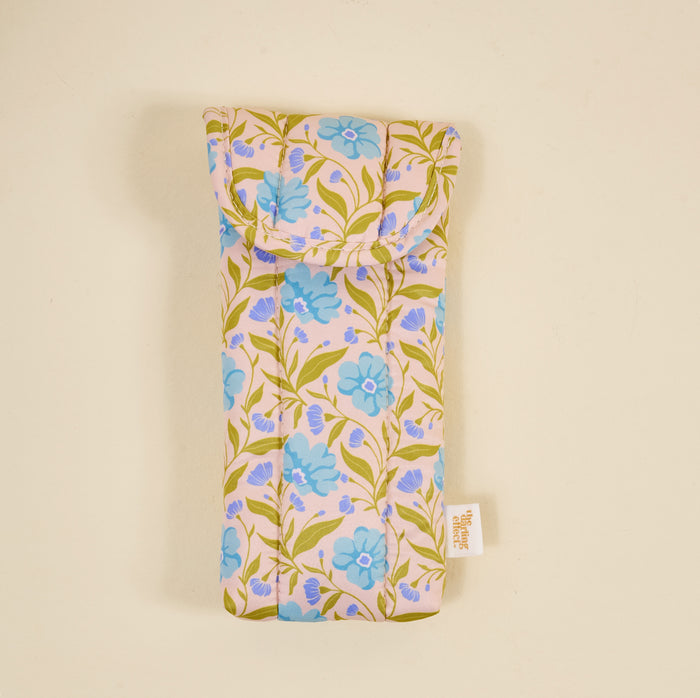The Darling Effect's Poppin' Petals Aqua Puffy Sunglasses Case is a soft, machine-washable quilted case featuring blue flowers and green leaves on light beige, displayed against a plain background.