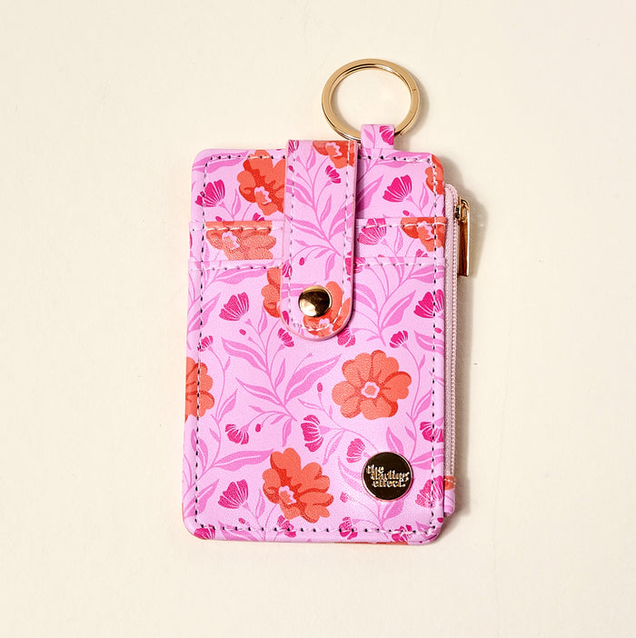 The Darling Effect Poppin' Petals Hot Pink Keychain Wallet features a pink floral pattern with red and orange flowers, gold keyring, snap strap, zip pocket, and a small metallic logo plate at the bottom right corner.