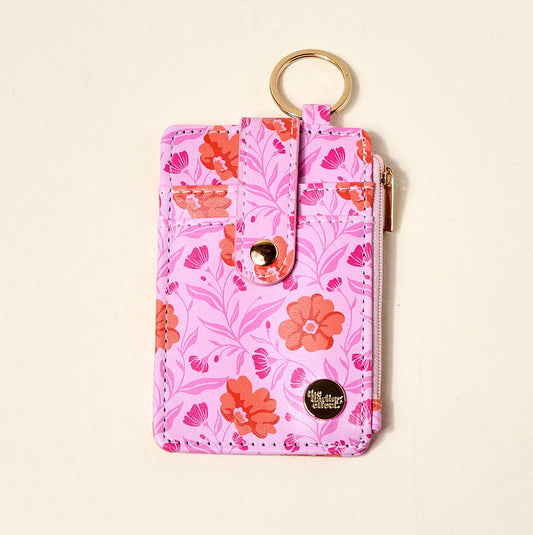The Darling Effect Poppin' Petals Hot Pink Keychain Wallet features a pink floral pattern with red and orange flowers, gold keyring, snap strap, zip pocket, and a small metallic logo plate at the bottom right corner.