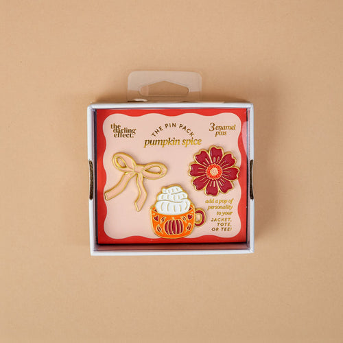 Introducing Pumpkin Spice The Pin Pack by The Darling Effect: a thoughtfully curated set displayed on a peach background, featuring three vibrant pins—a cheerful yellow bow, a cozy pumpkin spice latte, and a bright red flower. The packaging reads “pumpkin spice” and encourages you to add these collectible pins to your favorite jacket or tee.