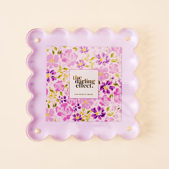 The Purple Square Scalloped Acrylic Frame by the-darling-effect features scalloped edges, pastel purple acrylic with magnetized panels, and encloses a floral print and “the darling effect” text. Holds a 4x4 photo in gold/black lettering.
