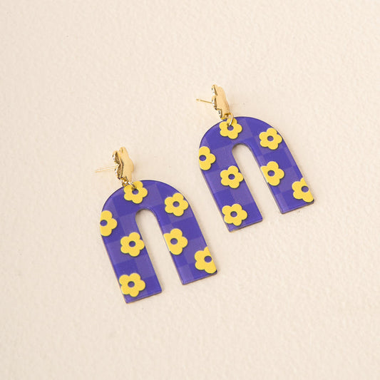 Show your school spirit with The Darling Effect’s Purple Yellow Game Day Acrylic Earrings—featuring a purple arch, yellow flowers, and checkered pattern, all stylishly set against a cream background.