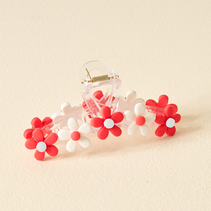 The Darling Effect’s Red Game Day Daisy Claw Clip features red and white daisy-shaped flowers—ideal for sporting your school colors or elevating your Game Day style, displayed on a light beige surface.