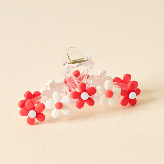 The Darling Effect’s Red Game Day Daisy Claw Clip features red and white daisy-shaped flowers—ideal for sporting your school colors or elevating your Game Day style, displayed on a light beige surface.