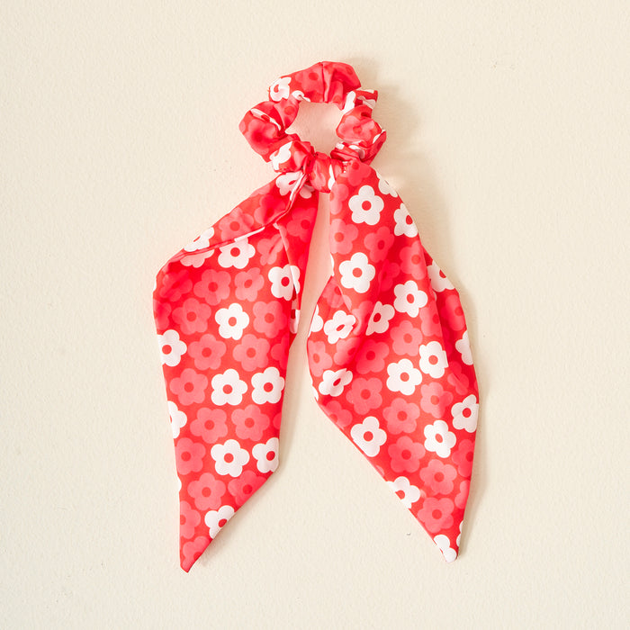 Display your team spirit with The Darling Effect’s Red Game Day Hair Scarf with Scrunchie—a red accessory featuring scarf-like ribbons and a white and pink daisy pattern, shown on a plain light background.