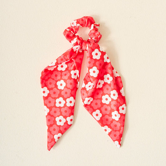 Display your team spirit with The Darling Effect’s Red Game Day Hair Scarf with Scrunchie—a red accessory featuring scarf-like ribbons and a white and pink daisy pattern, shown on a plain light background.