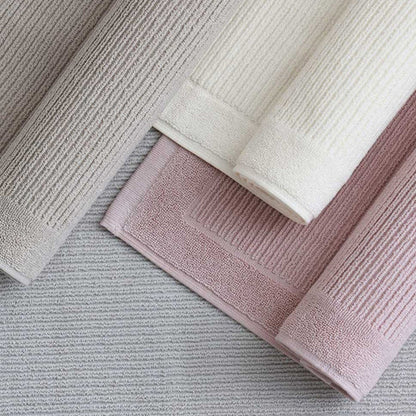 Three rolled-up textured Renew bath mats in various colors on a neutral background.