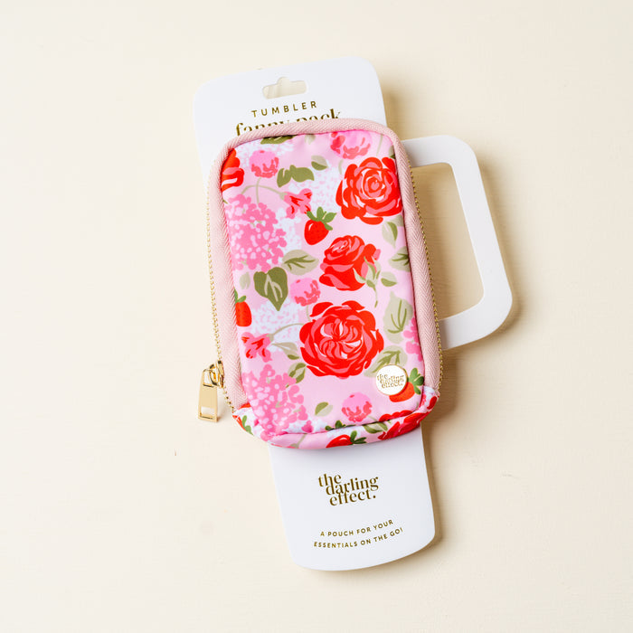 The Darling Effect Rose Garden Tumbler Fanny Pack is a stylish, small rectangular pink pouch with a red and pink floral pattern, gold zipper, water-resistant design, and comes attached to white packaging labeled Tumbler Fanny Pack.