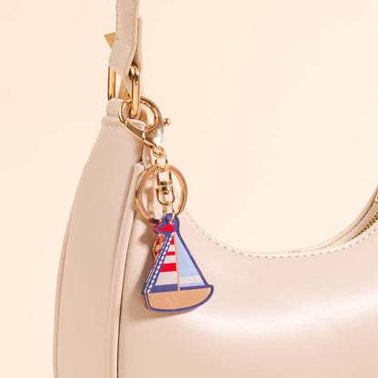 Add a nautical touch to your look with The Darling Effect Sailboat Acrylic Keychain, featuring a red, white, and blue sailboat charm on beige—perfect for accessorizing your cream leather handbag.