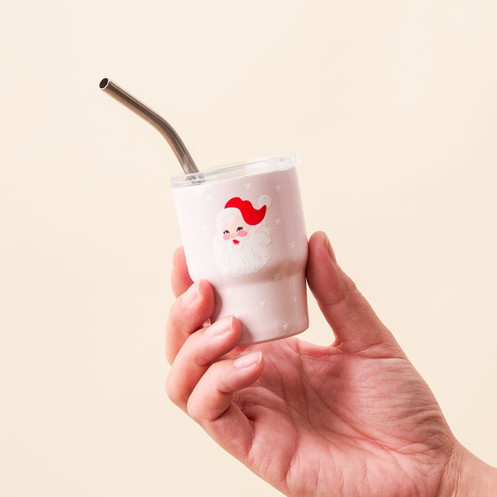 A hand holds The Darling Effect Santa 2 oz Tiny Tumbler, featuring a vintage Santa Claus design and a metal straw.