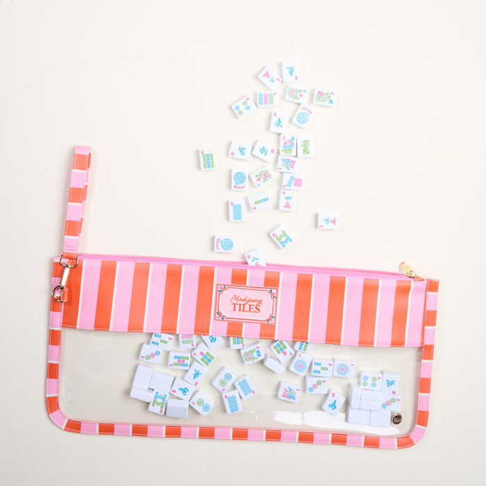 The Darling Effect's Sicily Stripes Pink Mahjong Tile Keeper Pouch, featuring pink and orange stripes, neatly stores small Mahjong tiles, with a few vibrantly scattered outside the organizer on a light surface.