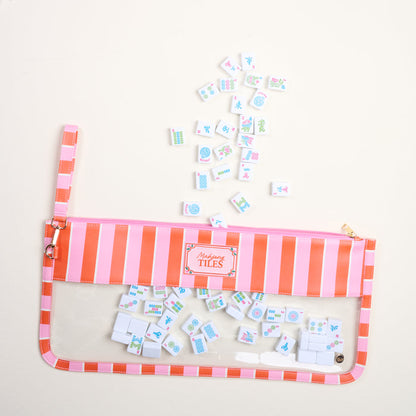 The Darling Effect's Sicily Stripes Pink Mahjong Tile Keeper Pouch, featuring pink and orange stripes, neatly stores small Mahjong tiles, with a few vibrantly scattered outside the organizer on a light surface.