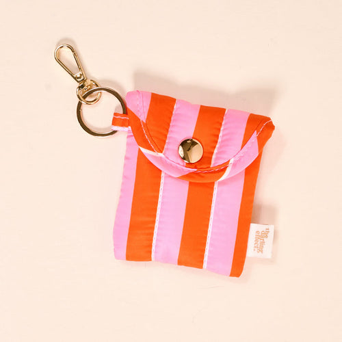 The Darling Effect Sicily Stripes Pink Puffy Earbud Case features pink and red vertical stripes, a snap button closure, a white side tag, and a gold keychain clasp on the corner.