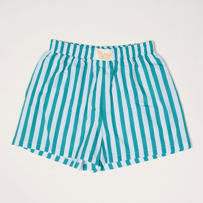 The Darling Effect Sicily Stripes Teal All Day Boxer Shorts feature vertical teal and light blue stripes, breathable fabric, an elastic waistband, and a white label with orange text. They're laid flat on a white background for a trendy look.