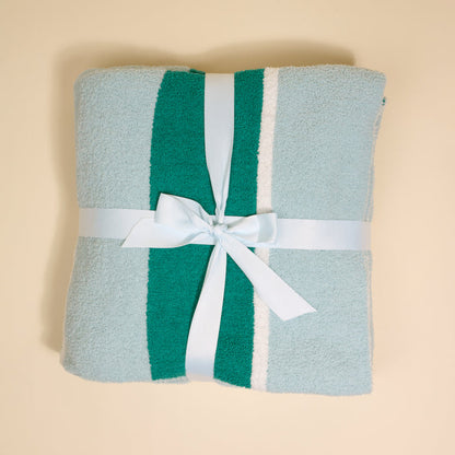 The Darling Effect’s Sicily Stripes Teal Cozy Dreams Luxe Blanket features light blue, teal, and white stripes, folded neatly with a matching ribbon on a beige surface—ultra-soft for maximum comfort.