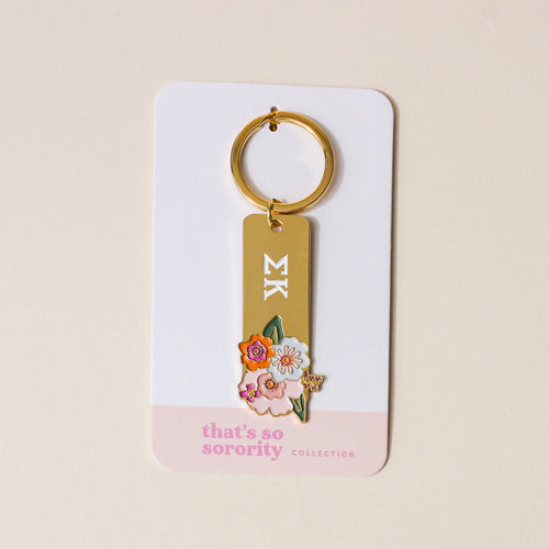 The Darling Effect’s Sigma Kappa Enamel Keychain features white ΣΚ Greek letters and colorful flowers on gold enamel, attached to a “thats so sorority COLLECTION” card—making it a perfect Sigma Kappa gift.