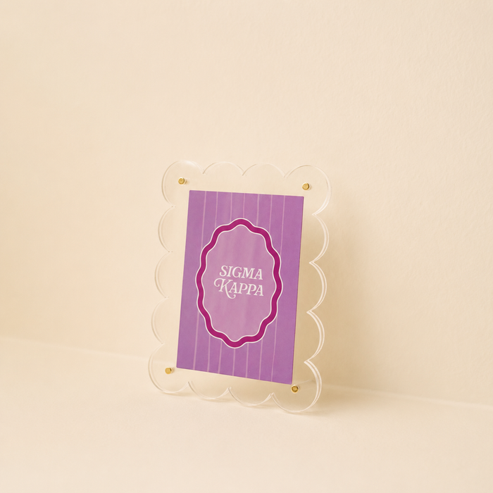The Darling Effect’s Sigma Kappa Mini Acrylic Picture Frame Magnet features a small, scalloped-edge clear acrylic frame displaying a purple, vertically striped card with SIGMA KAPPA in white on a beige background.
