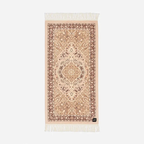 Slowtide Haven Beach Towel in Fawn features ornate central motif, floral border, and white fringe trim at both ends.