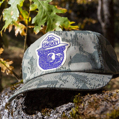 Forager Provisions LTD Smokey Bear vintage logo repair patch applied to a camouflage cap in a forest setting.