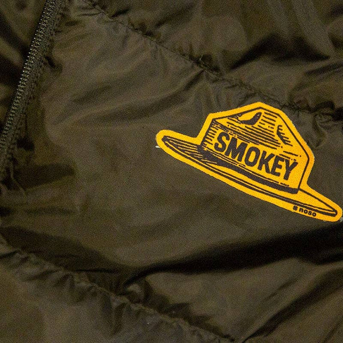 Forager Provisions LTD Smokey Bear ranger hat repair patch applied to a dark green quilted outdoor jacket.