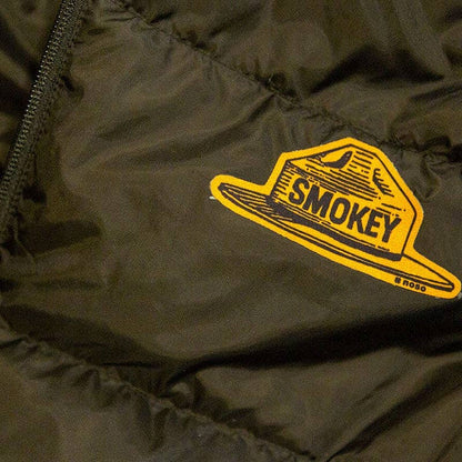 Forager Provisions LTD Smokey Bear ranger hat repair patch applied to a dark green quilted outdoor jacket.