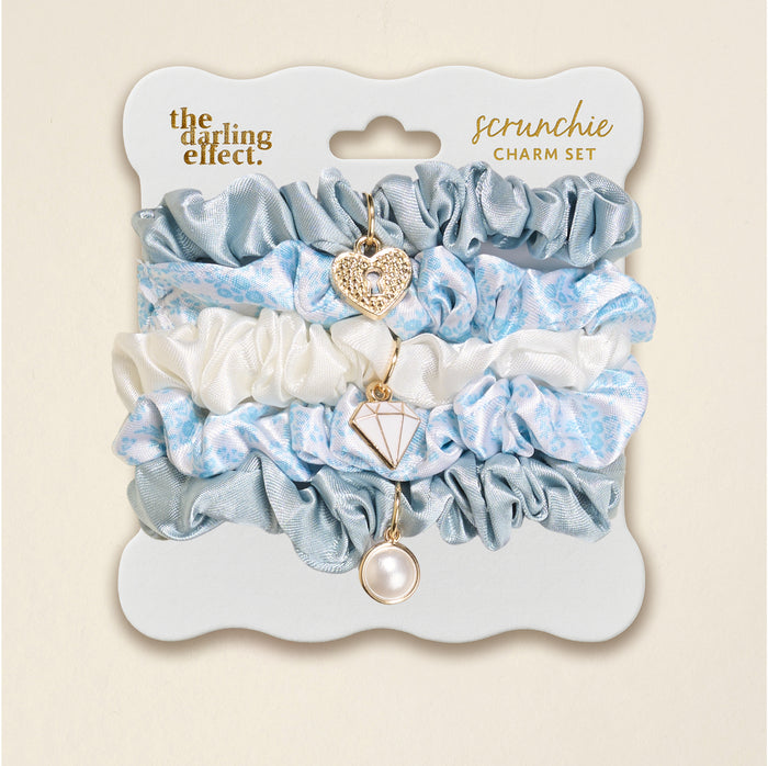 The Darling Effect’s Something Blue Scrunchie Charm Set includes light blue satin, white floral, and blue scrunchies, each with a dangling heart, diamond, or pearl charm—perfect for adding flair to any hairstyle.