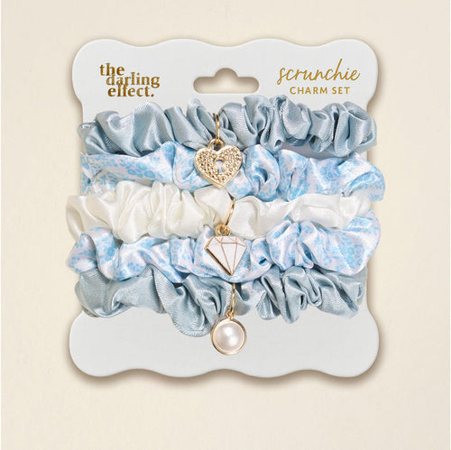 The Darling Effect’s Something Blue Scrunchie Charm Set includes light blue satin, white floral, and blue scrunchies, each with a dangling heart, diamond, or pearl charm—perfect for adding flair to any hairstyle.