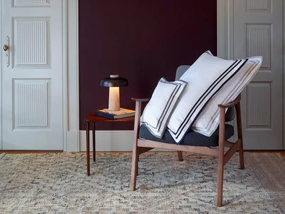 Chair with sonata white sand and white midnight pillowcase sham in a room with a dark wall and wooden floor.