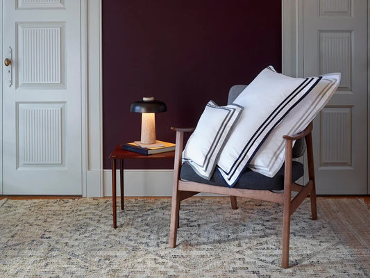 Chair with sonata white sand and white midnight pillowcase sham in a room with a dark wall and wooden floor.