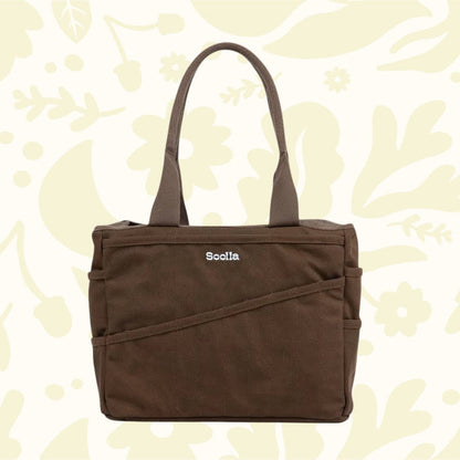 Soolla Studio Pottery Artist Bag in Coffee Bean with two handles, displayed on a light floral background for stylish storage.
