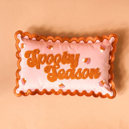 The Darling Effect Spooky Season Scalloped Rectangle Throw Pillow features pink fabric, orange scalloped edges, and textured orange “Spooky Season” lettering with candy corn accents—a playful addition to any sofa or pillow set.