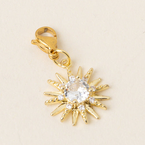 The-darling-effect’s Star Burst Jewelry Charm Gold features a gold sun design with a clear crystal center and sparkling rays, plus an easy-attach clasp—perfect for your charm bar.