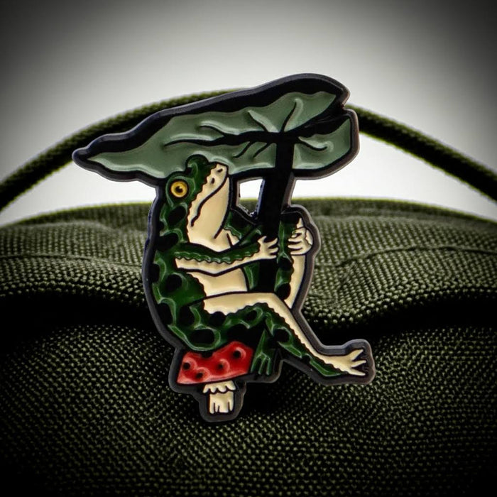 Forager Provisions LTD Stay Home Club enamel pin featuring a green frog holding a leaf umbrella while sitting on a mushroom