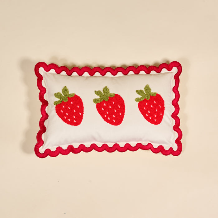 The Darling Effect Strawberries Scalloped Rectangle Throw Pillow features three red strawberries with green leaves and a wavy red border, adding charm to any cozy home decor when placed on a beige background.