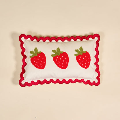 The Darling Effect Strawberries Scalloped Rectangle Throw Pillow features three red strawberries with green leaves and a wavy red border, adding charm to any cozy home decor when placed on a beige background.