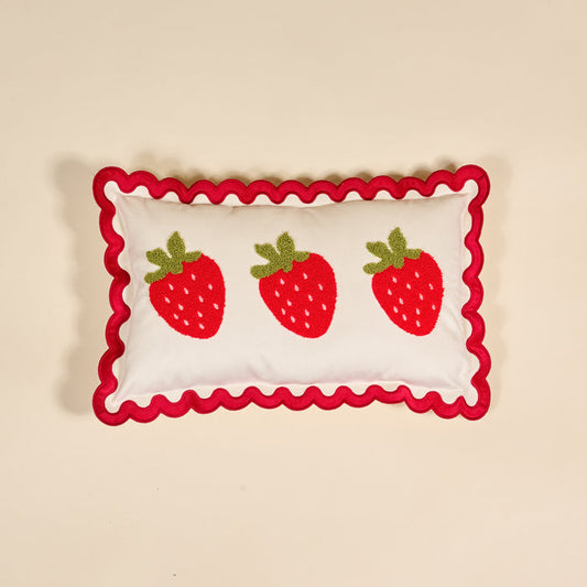 The Darling Effect Strawberries Scalloped Rectangle Throw Pillow features three red strawberries with green leaves and a wavy red border, adding charm to any cozy home decor when placed on a beige background.