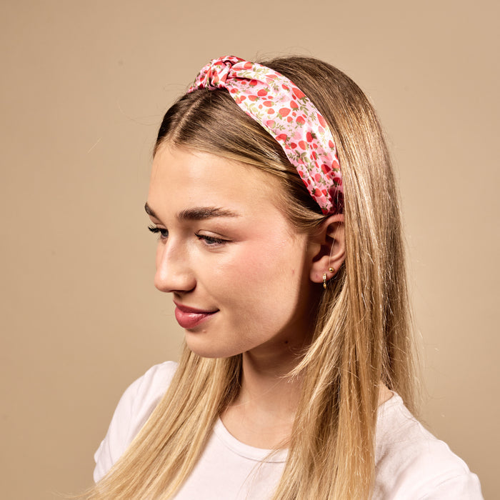 A young woman with long blonde hair wears The Darling Effect's Strawberry Fields Classic Twist Headband, styled with a white t-shirt and small gold earrings.