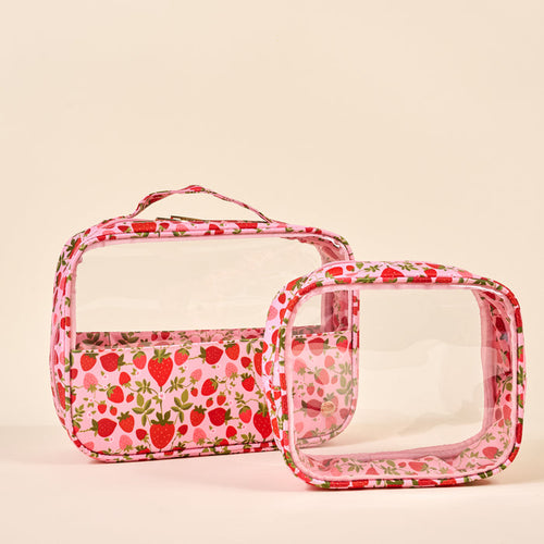 The Darling Effect Strawberry Fields Clearly Chic Cosmetic Bag Set features two upright rectangular clear bags with pink borders and strawberry prints—one large with a handle, one small—ideal for travel toiletries or everyday cosmetics.