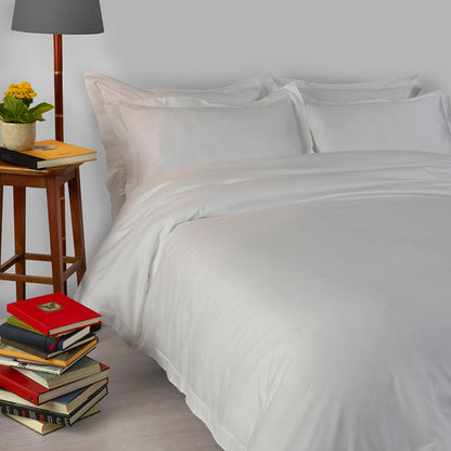 Suave-CoolGrey pillowcase and duvet cover on a bed with a stack of books and a lamp in the background.